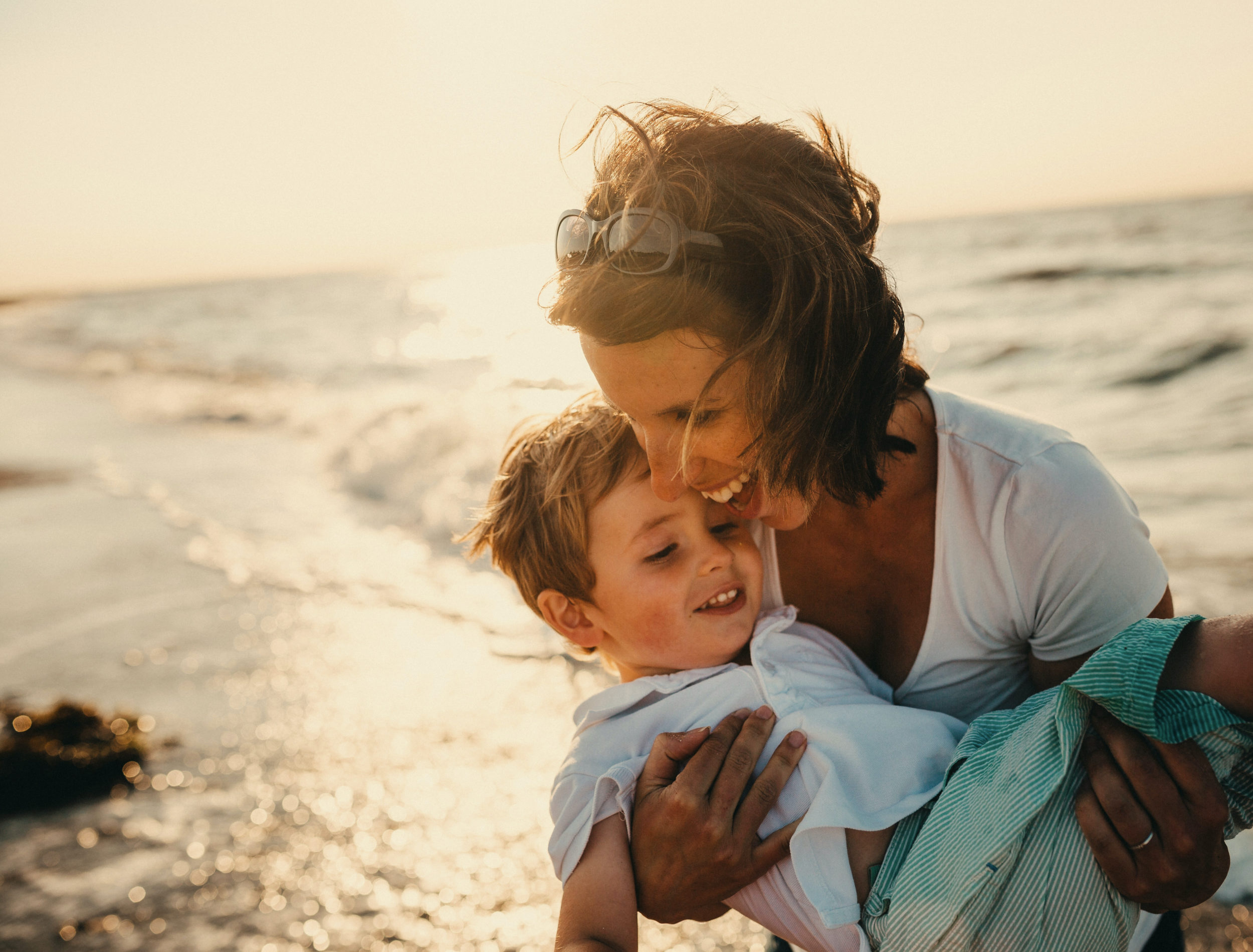 Photo d'une maman qui rigole avec son bébé dans les bras sur la plage