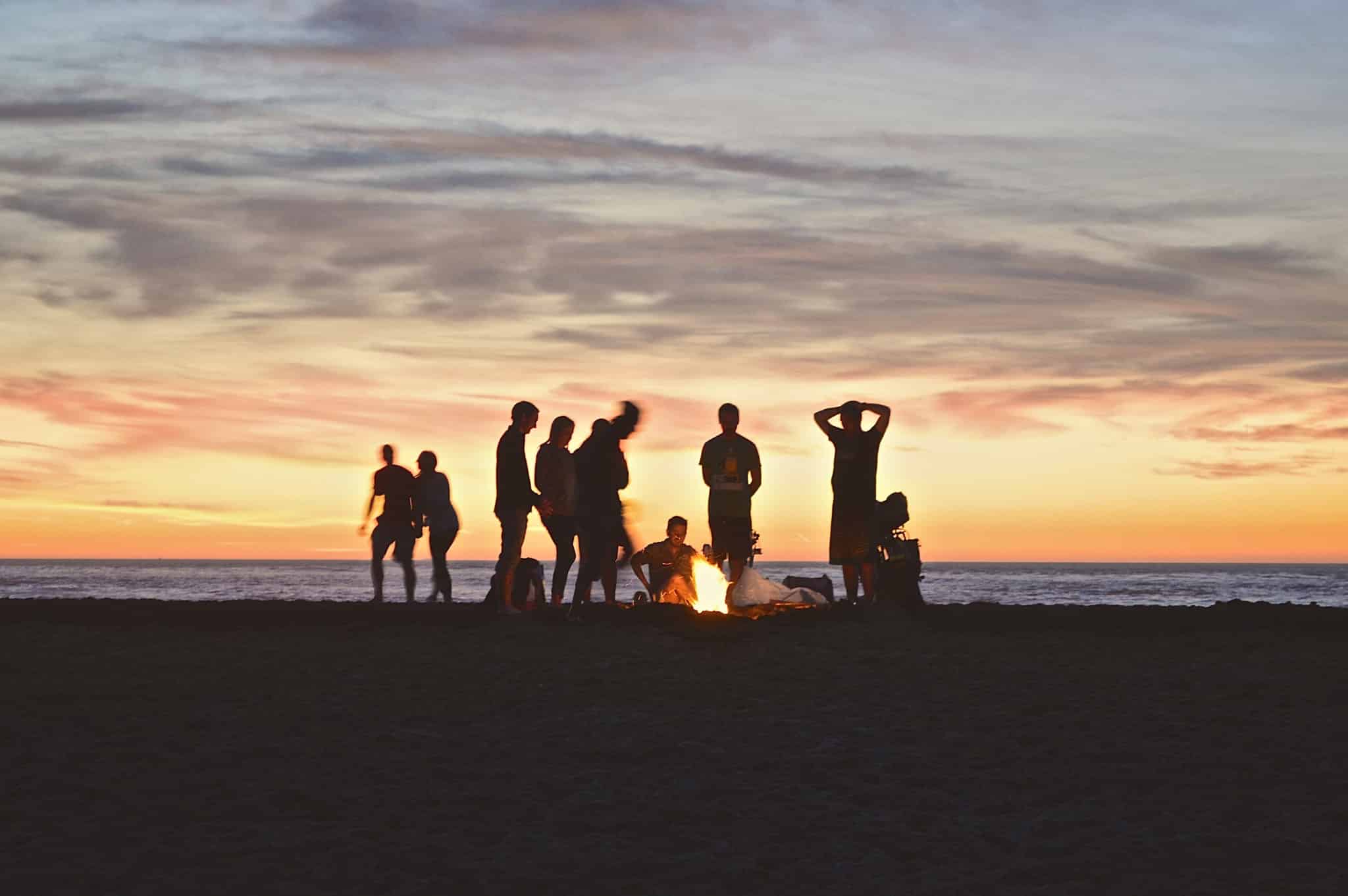 Photo d'un groupe de personnes sur la plage au couché du soleil avec un feu de camp