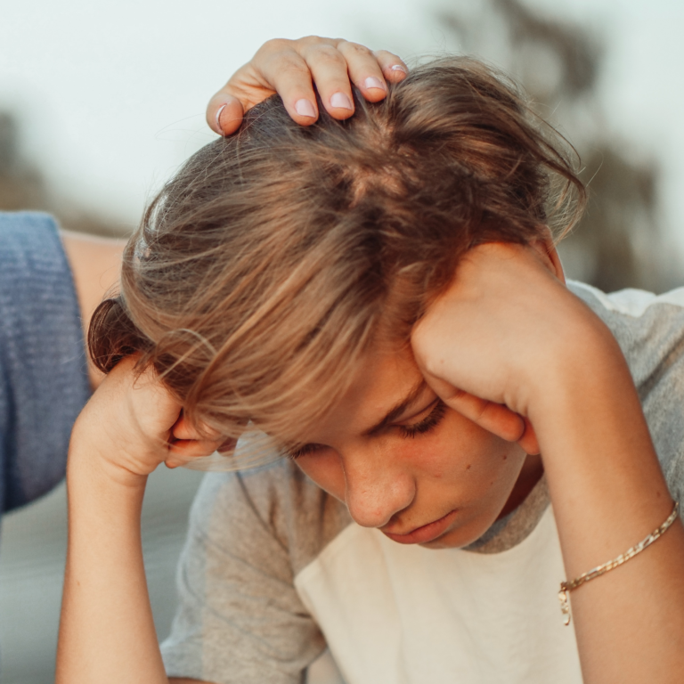 Photo d'un adolescent qui à l'air triste avec sa mère qui pose sa main sur sa tête