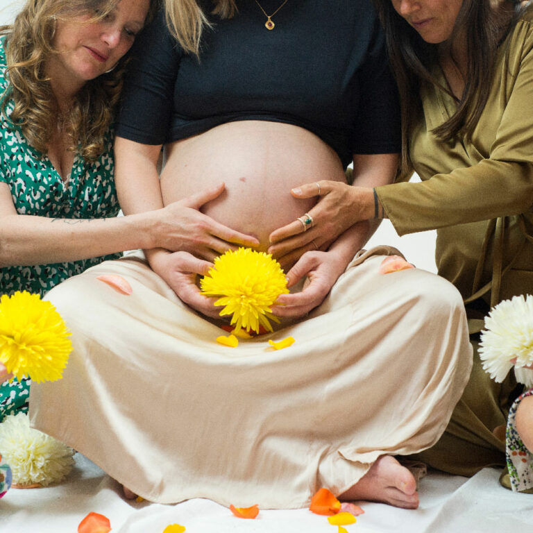 Mother blessing - Photo d'un femme enceinte avec des fleurs et deux femmes à côté d'elle qui lui touche le ventre